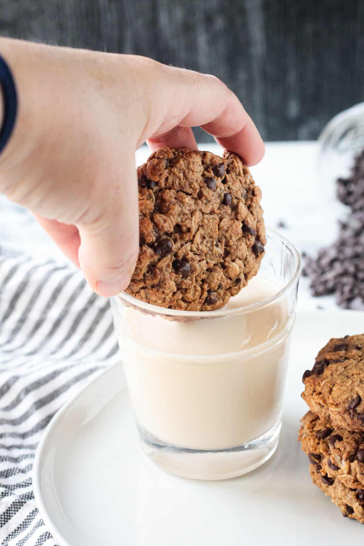 Adult hand dunking a cookie into a glass of milk.