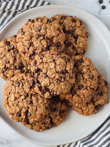Overhead view of a pile of vegan oatmeal chocolate chip cookies on a plate.