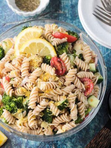 Bowl of vegan pasta salad with rotini noodles, broccoli, cucumber, artichokes, and tomatoes.