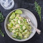 Vegan quinoa salad with green veggies and fruit on a gray plate.