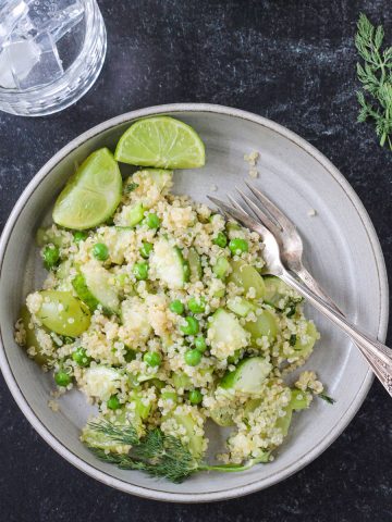 Vegan quinoa salad with green veggies and fruit on a gray plate.