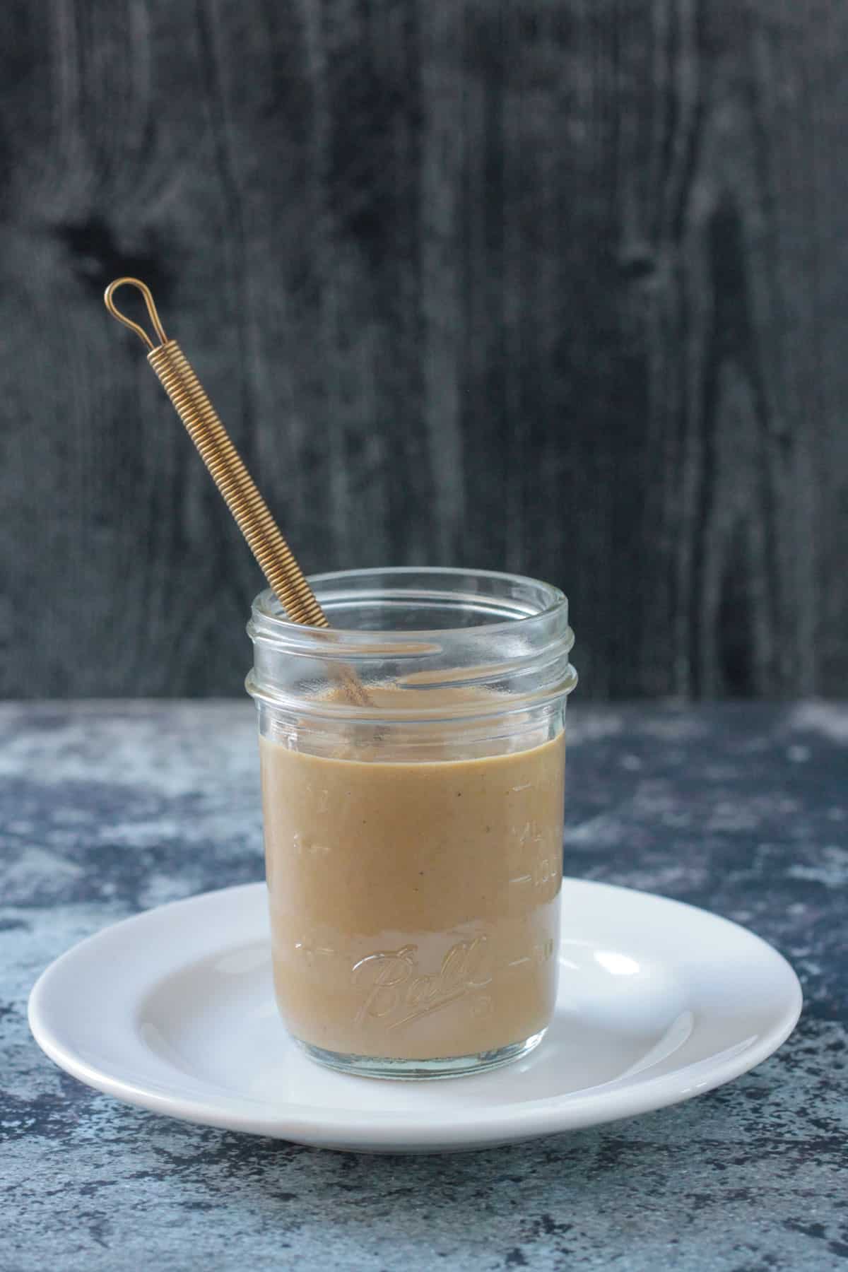 Tahini dressing in a glass jar with a gold colored metal whisk.