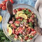 Two wooden serving spoons in a bowl of cucumber chickpea salad.