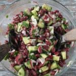 Beans, cucumbers, radishes, red onion, and fresh parsley mixed in a glass bowl.