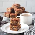 Stack of two cake squares on a white plate next to a cup of coffee.