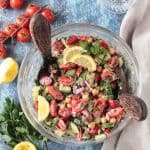 Two wooden serving spoons in a bowl of cucumber chickpea salad.