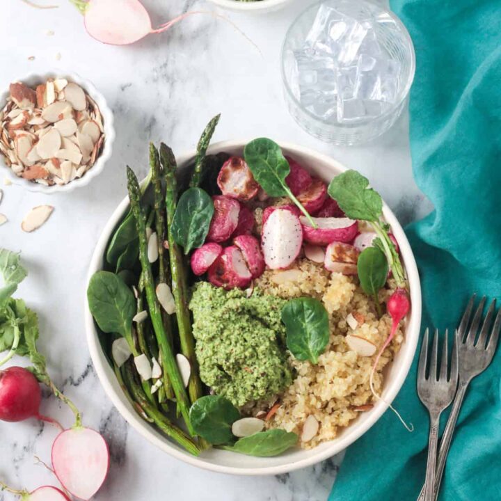 Quinoa veggie bowl with asparagus, radishes, fresh spinach, and pesto in a white flat bowl.