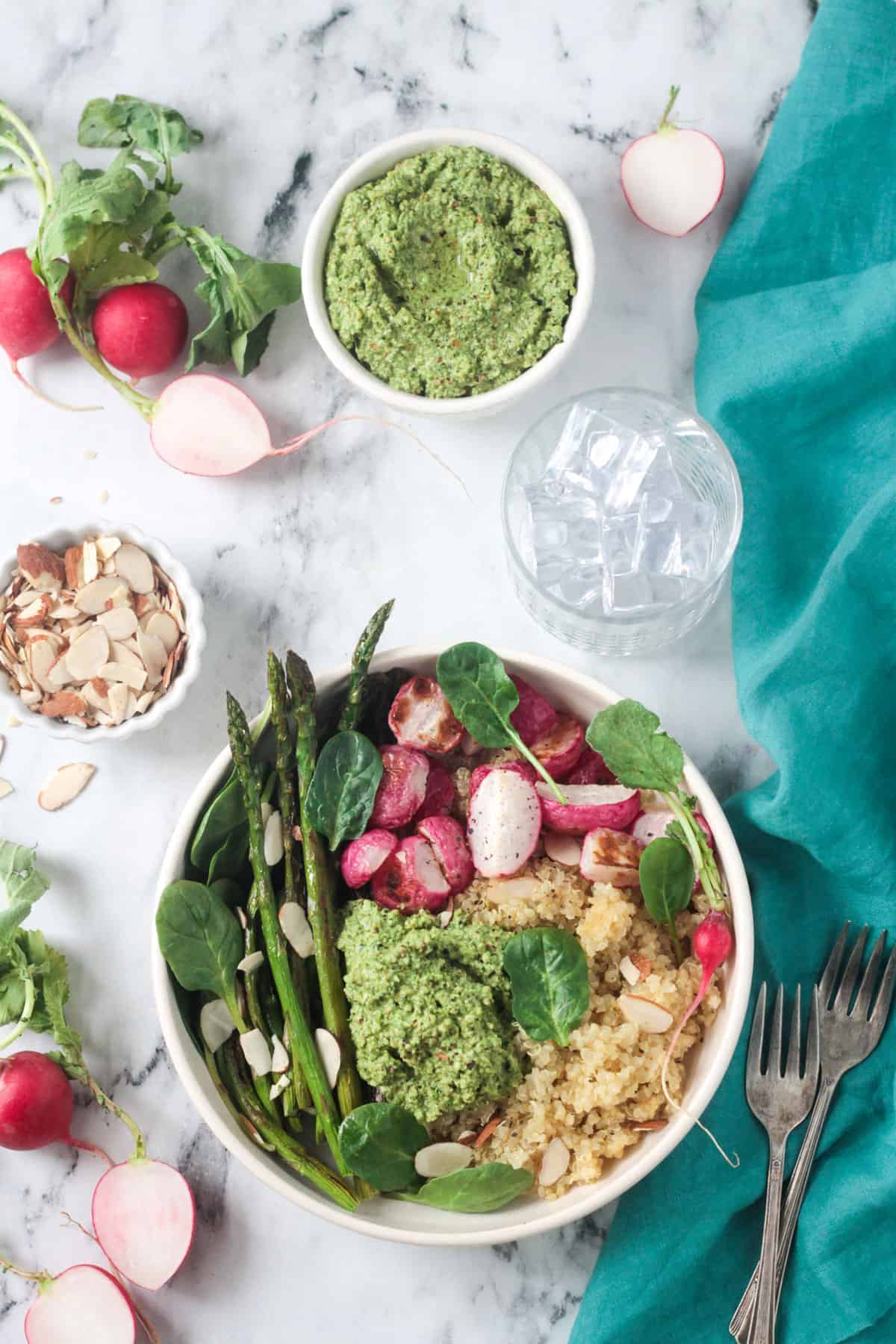 Quinoa veggie bowl with asparagus, radishes, fresh spinach, and pesto in a white flat bowl.