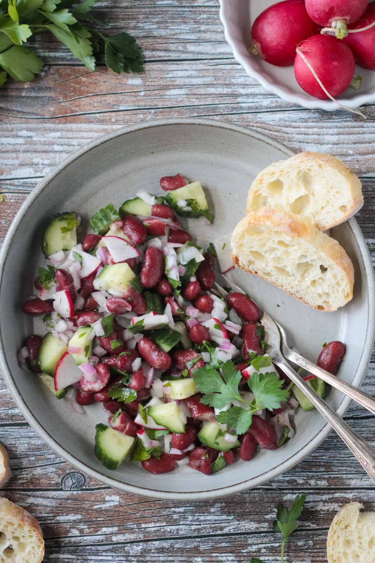 Red kidney bean salad on a gray plate with a baguette slice.