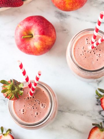 Overhead view of two glasses filled with strawberry smoothies on a white marble counter.