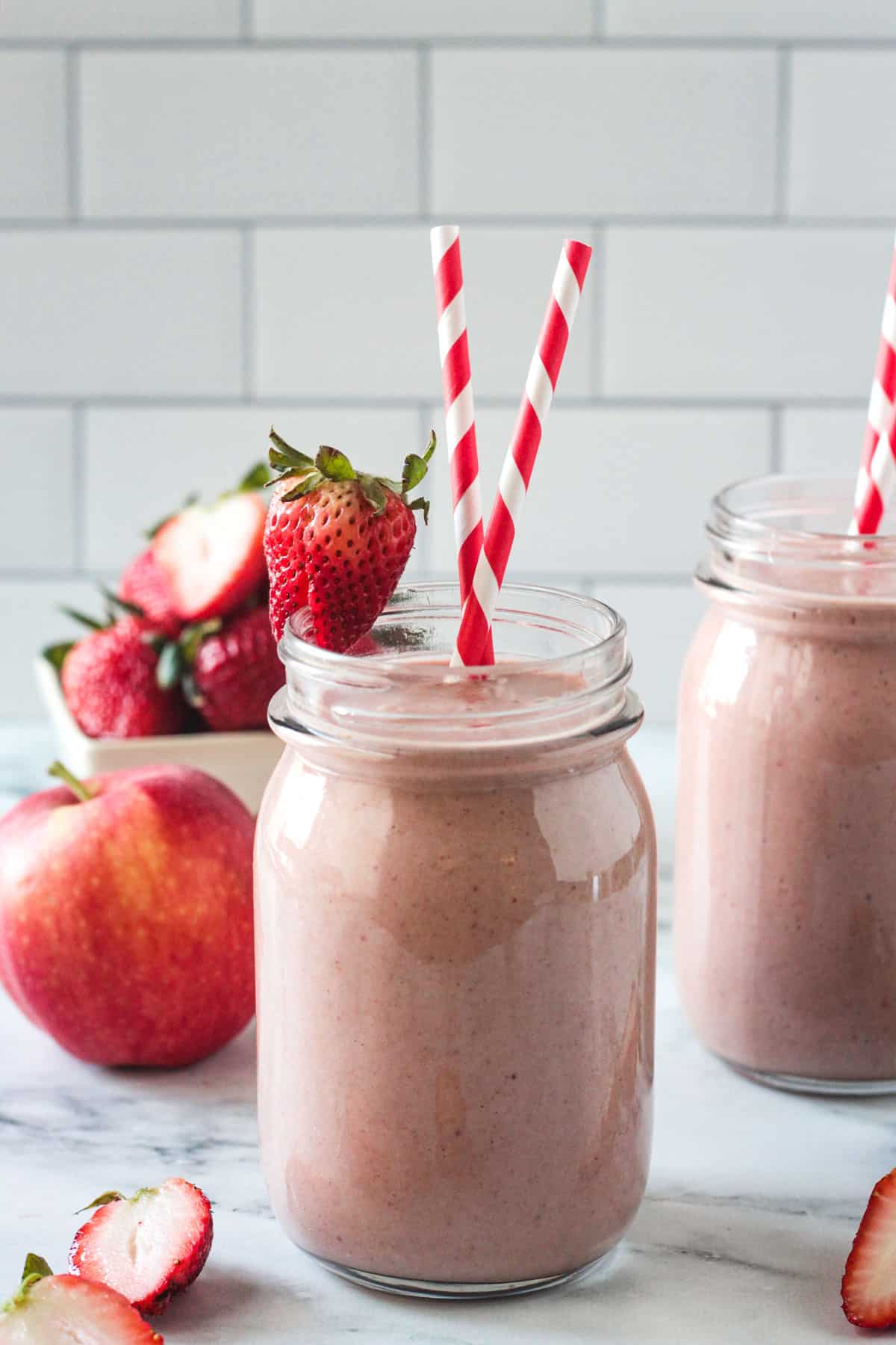 Strawberry Apple Smoothie in a glass with two red and white striped straws.