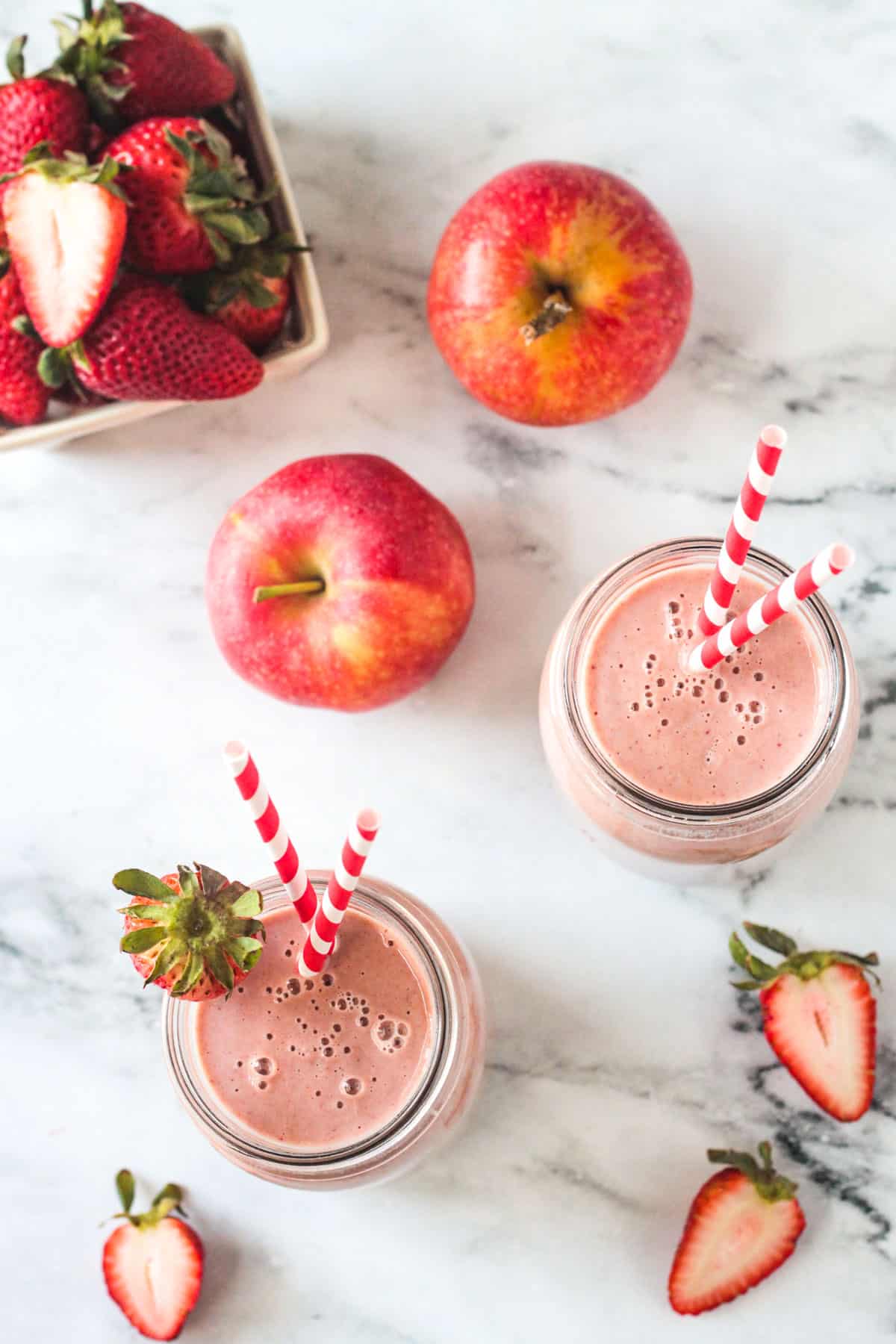 Overhead view of two glasses filled with strawberry smoothies on a white marble counter.