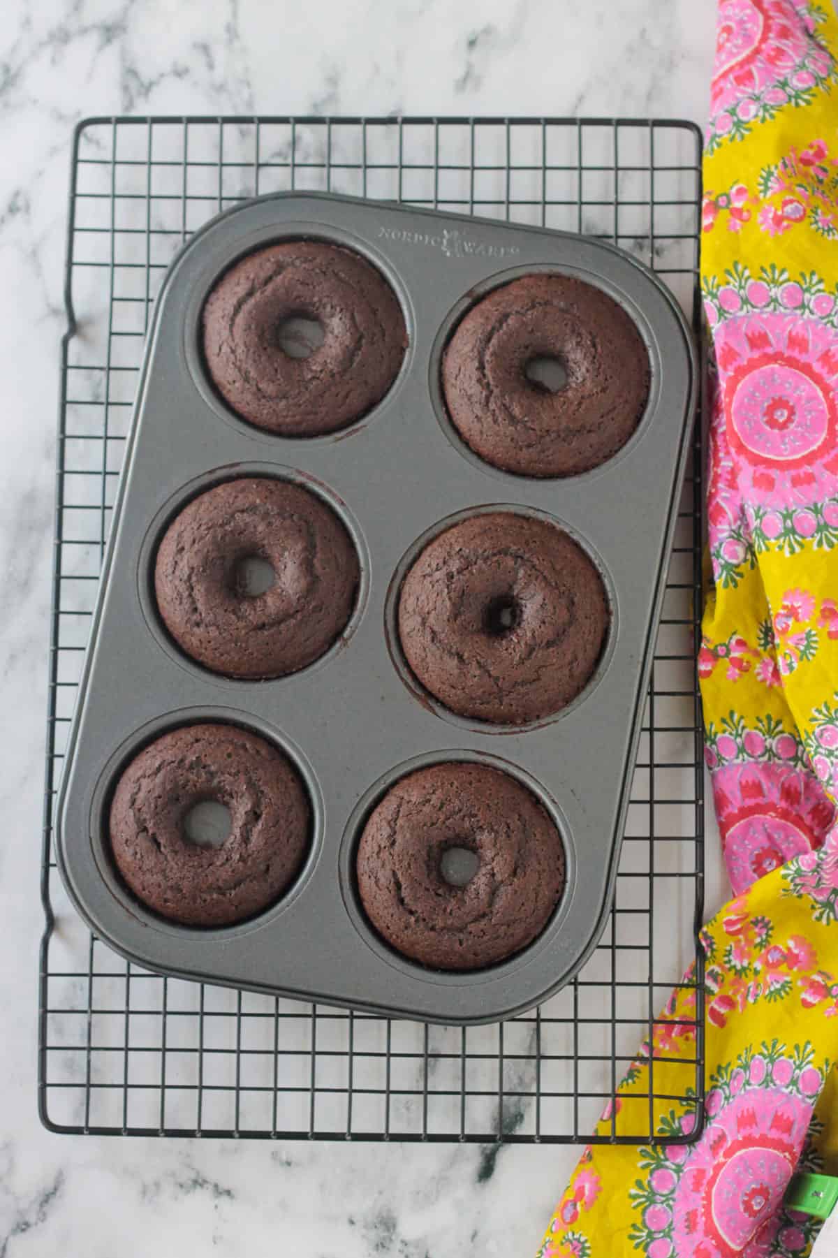 Finished donuts in a donut pan on a cooling rack.