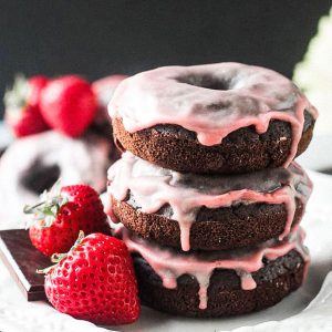 Stack of three vegan chocolate donuts with pink strawberry glaze.