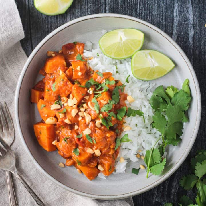 Sweet potato peanut butter curry with jasmine rice garnished with cilantro and two lime wedges.