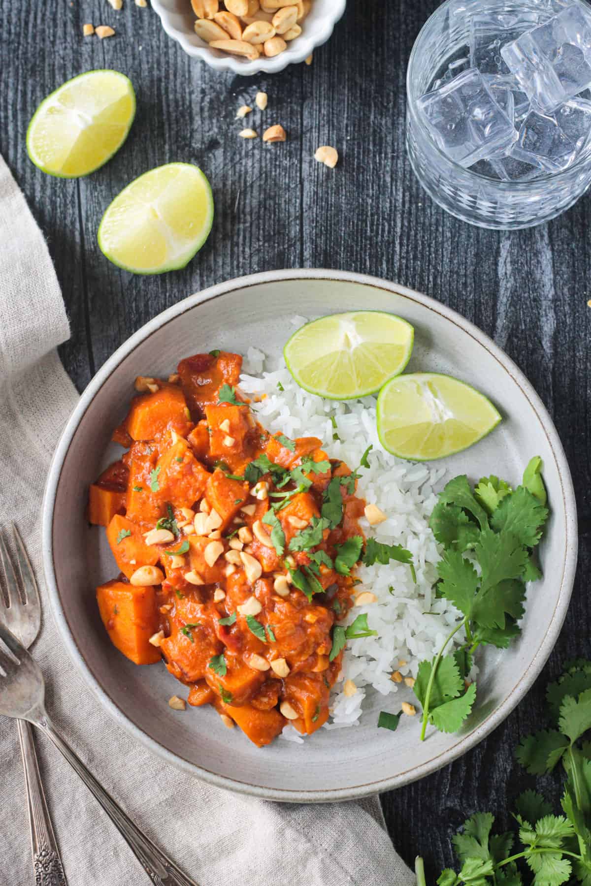 Sweet potato peanut butter curry with jasmine rice garnished with cilantro and two lime wedges.