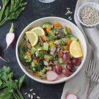 Raw Veggie Chopped Salad in a white bowl garnished with two lemon wedges.