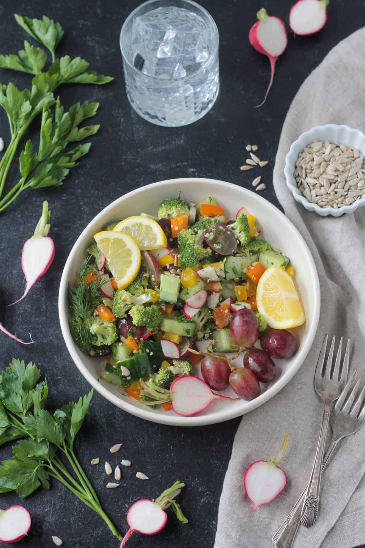 Raw Veggie Chopped Salad in a white bowl garnished with two lemon wedges.