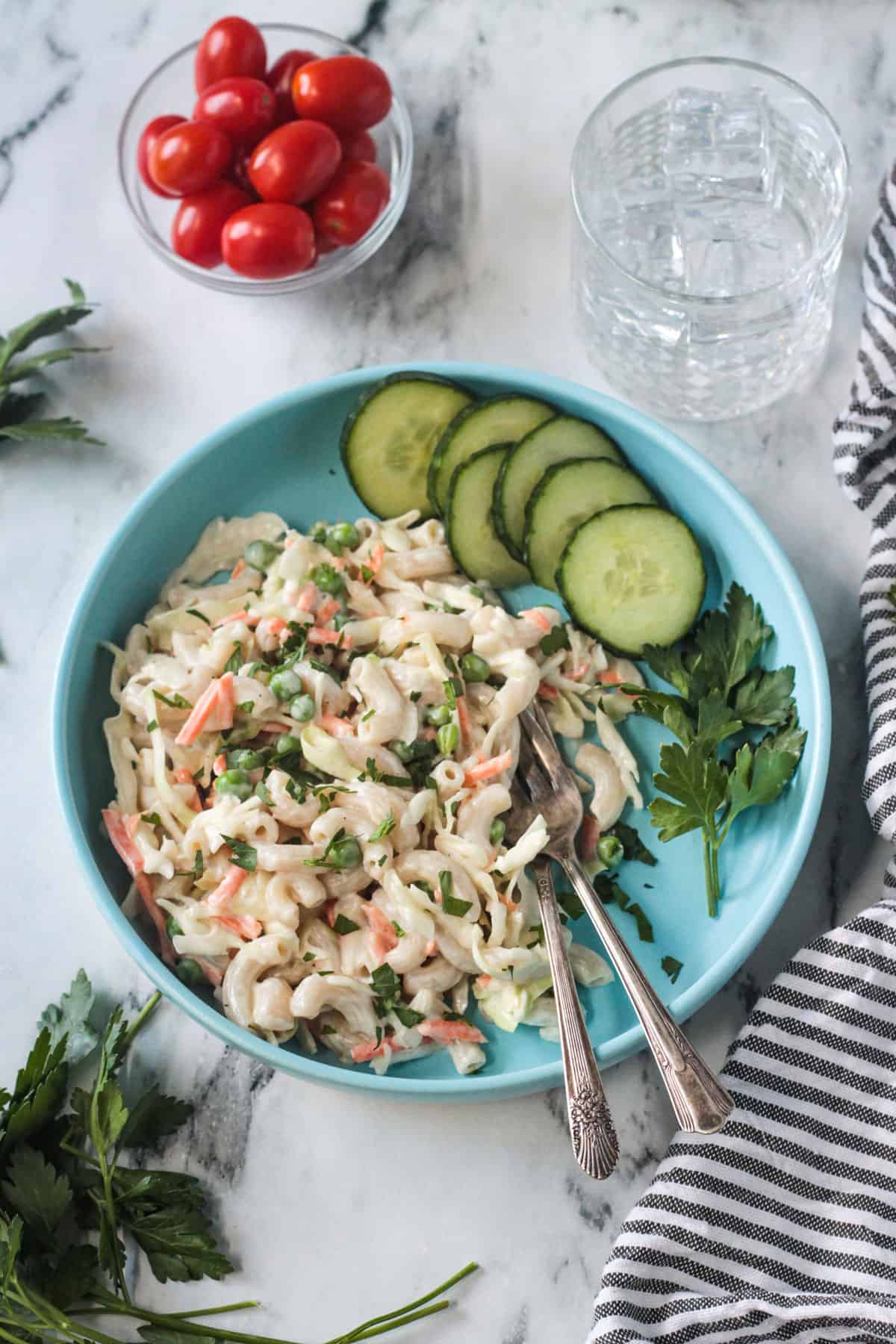 Vegan Macaroni Salad on a blue plate with two forks and a side of sliced cucumbers.