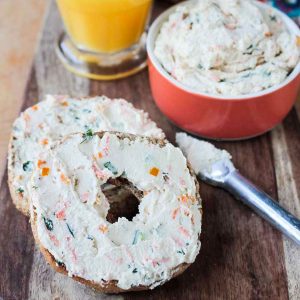 Two bagel halves topped with veggie cram cheese on a wooden platter.