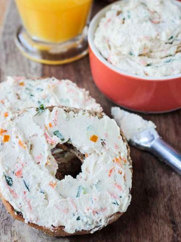 Two bagel halves topped with veggie cram cheese on a wooden platter.