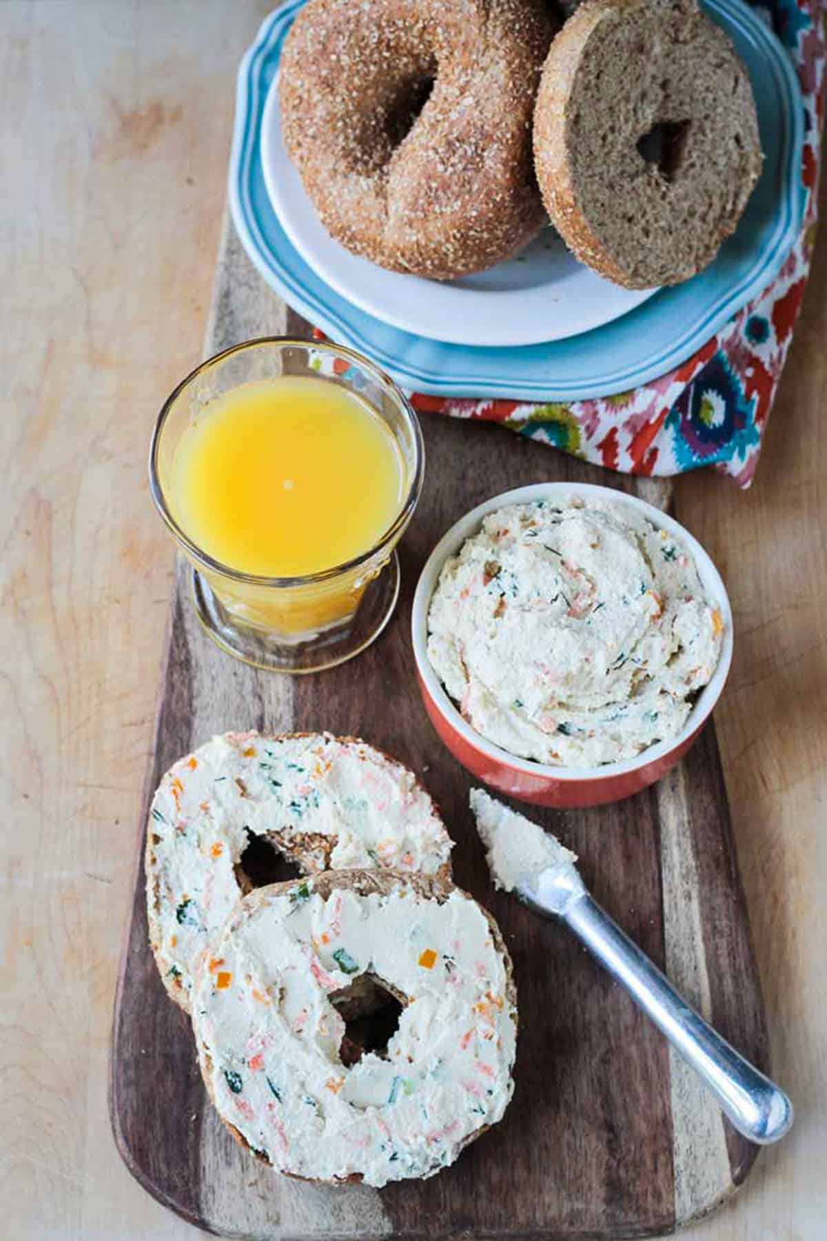 Plate of bagels next to a glass or orange juice and two bagel halves with veggie spread.