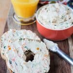 Two bagel halves topped with veggie cram cheese on a wooden platter.