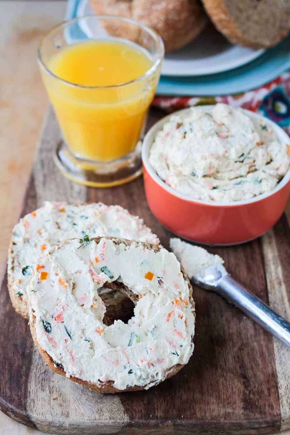 Two bagel halves topped with veggie cram cheese on a wooden platter.