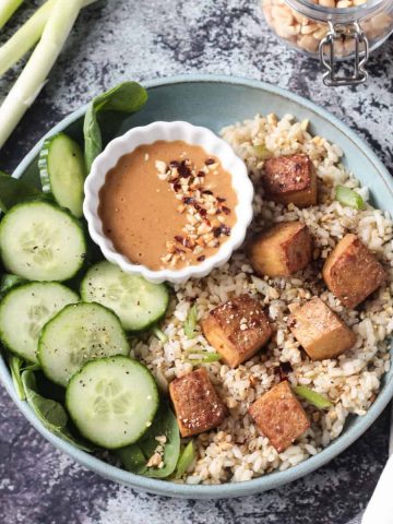 Oven baked tofu finished dish with rice, cucumbers, and sauce.