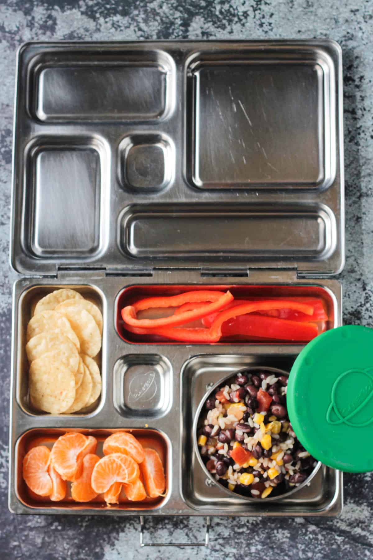 Bento style lunch box: rice and beans, orange slices, tortilla chips, red pepper slices.