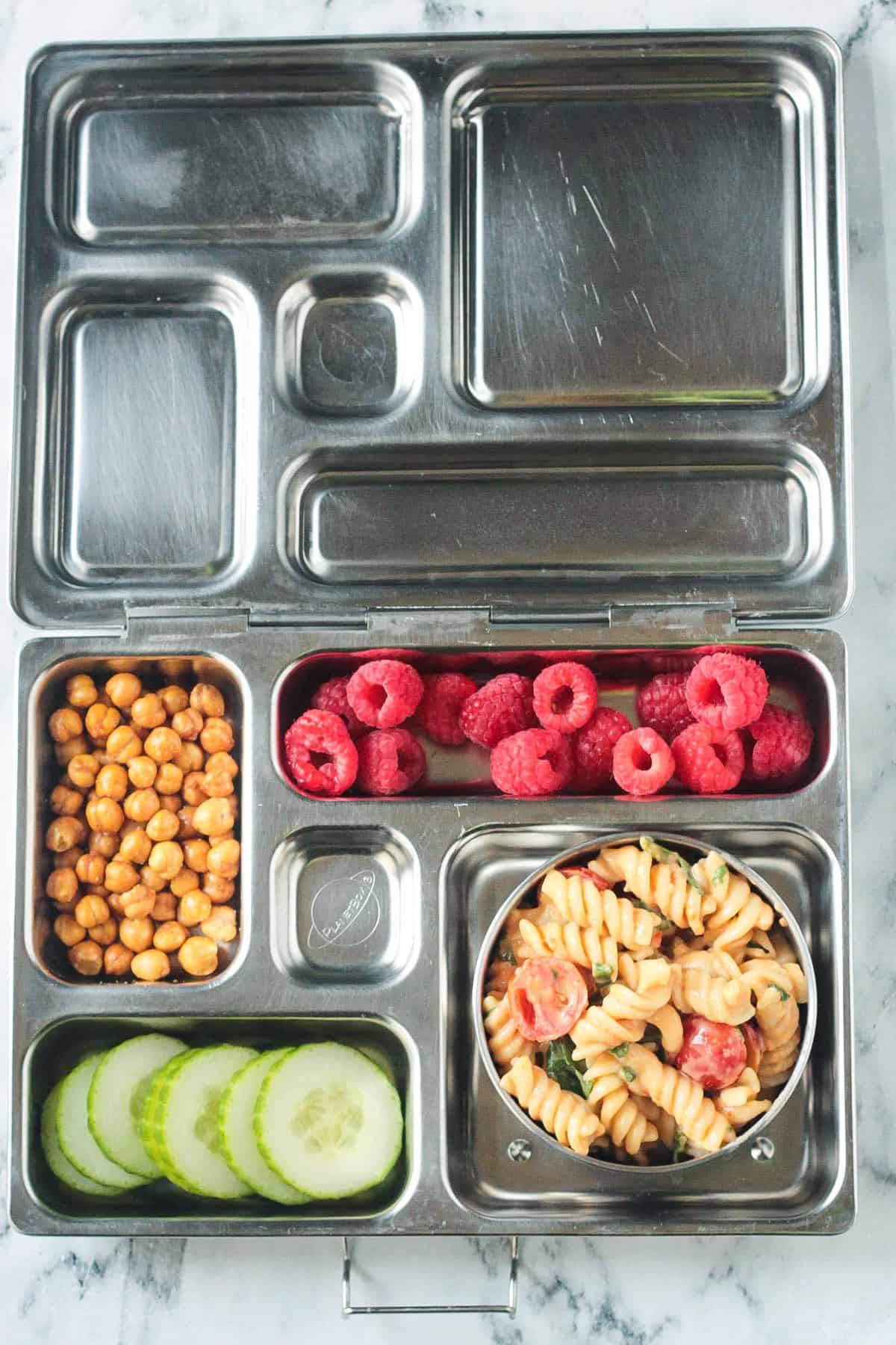 Bento style lunchbox with pasta salad, cucumbers, chickpeas, and raspberries.