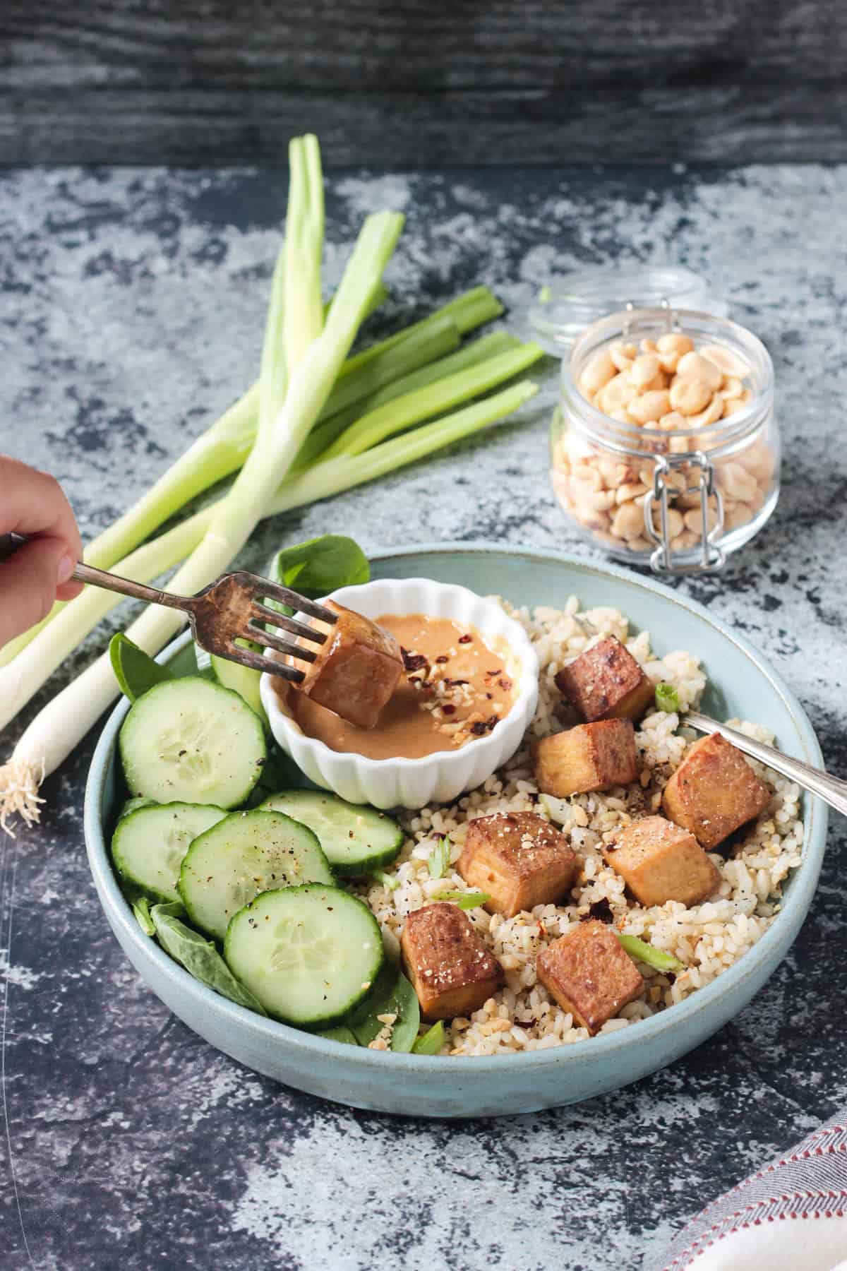 Bite of baked tofu being dipped into a small bowl of peanut sauce.