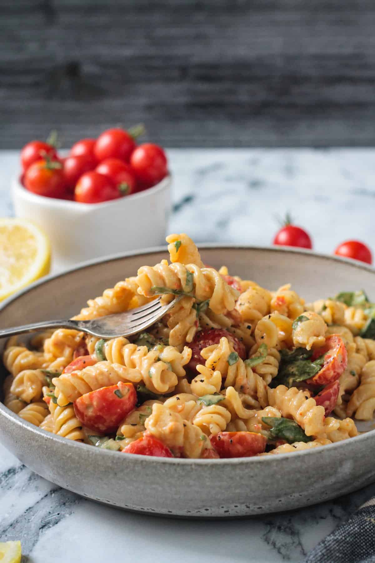 Two rotini noodles with sauce on a fork over a bowl of pasta.