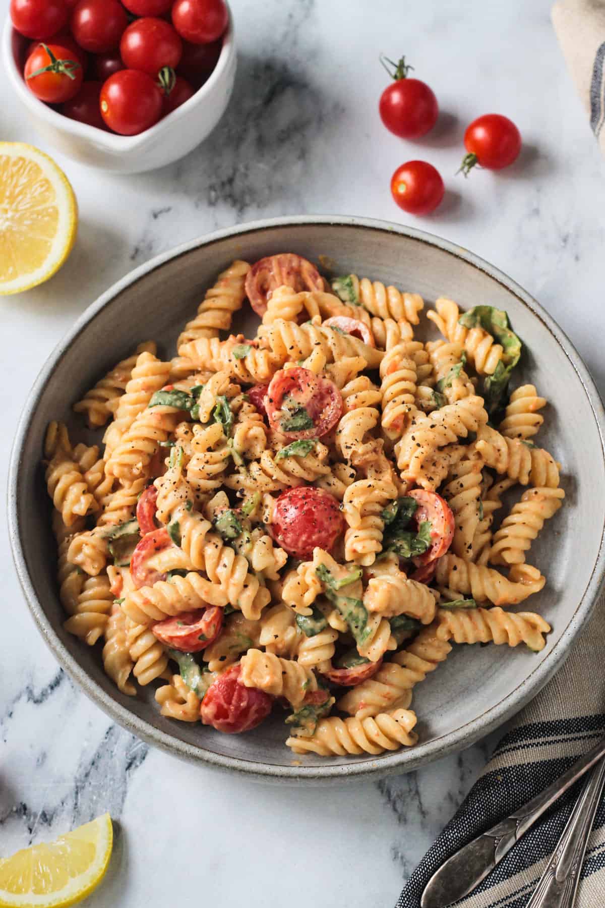 Rotini pasta in creamy sauce with tomatoes and spinach in a gray flat bowl.