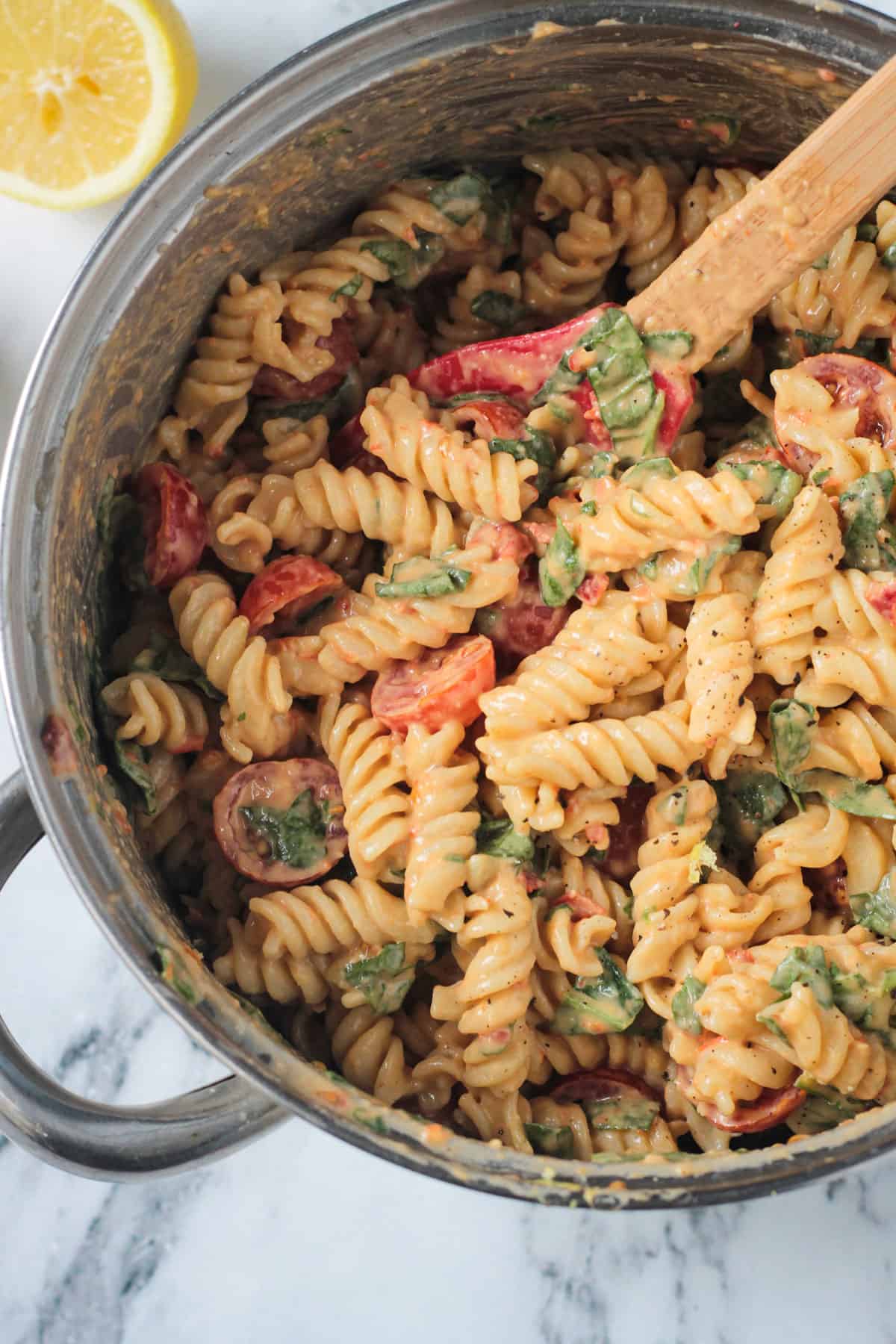 Red spatula stirring noodles in a pot with sauce, tomatoes, & spinach.