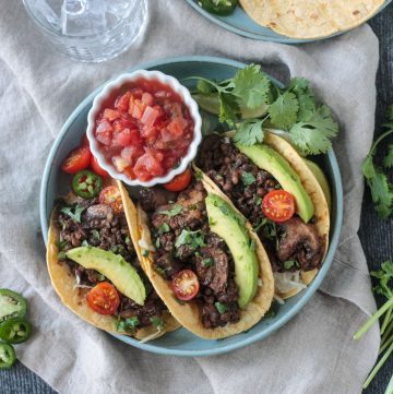 Three vegan lentil tacos with mushrooms and toppings next to a small bowl of salsa.
