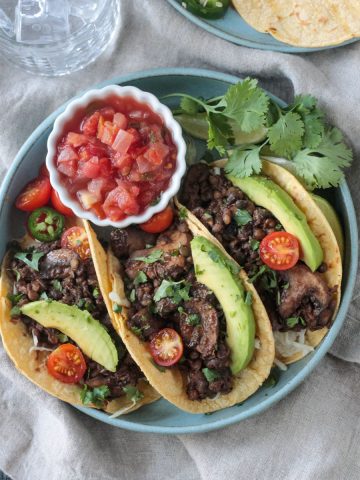 Three vegan lentil tacos with mushrooms and toppings next to a small bowl of salsa.