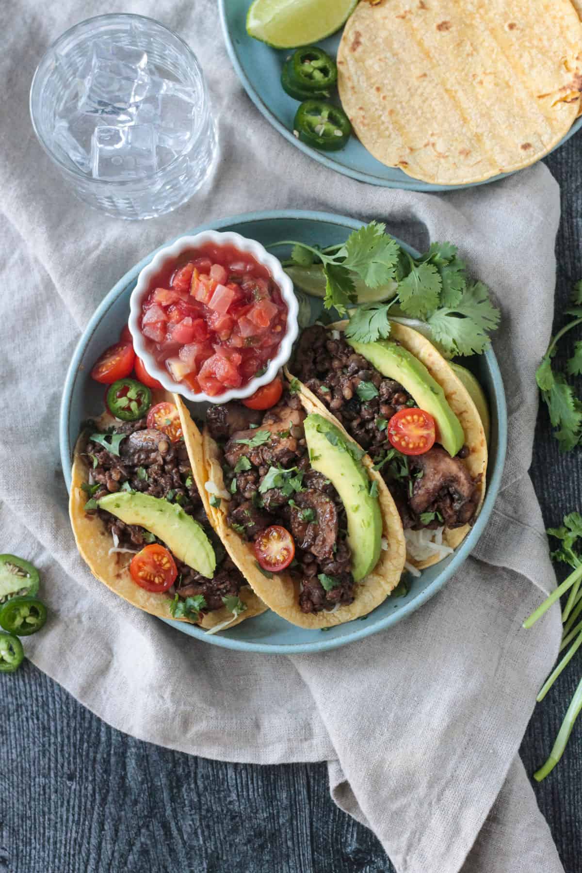 Three vegan lentil tacos with mushrooms and toppings next to a small bowl of salsa.