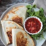 Overhead view of three halved vegan quesadillas next to a small bowl of salsa.