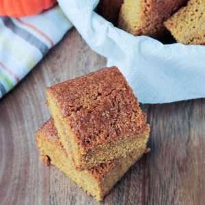 Two squares of dairy free cornbread stacked in front a basket of more.