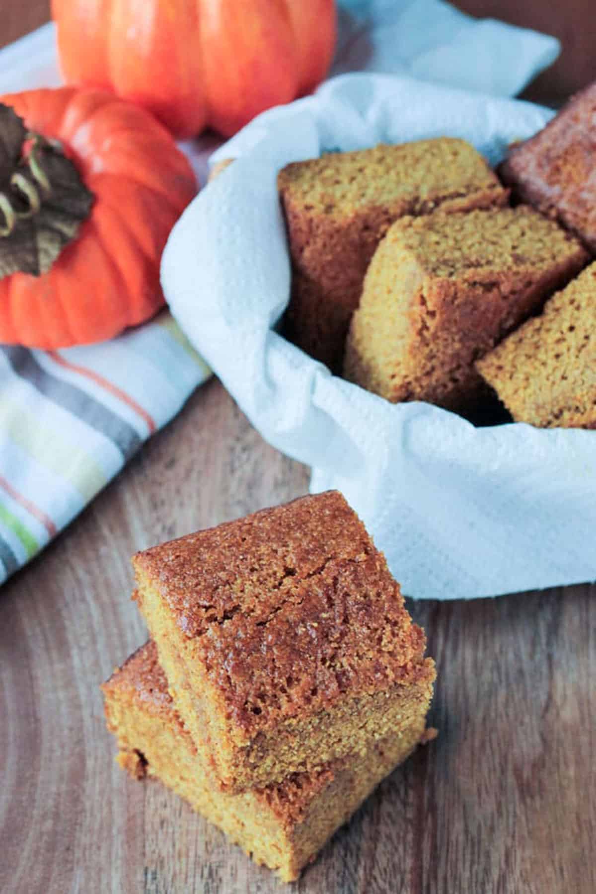 Pumpkin Maple Cornbread - a little sweet and super moist. Tastes almost more like cake than cornbread. Perfect for Thanksgiving or next to a bowl of soup or chili! It even makes a great snack. Can easily be made into muffins. Vegan and oil free! Two squares of dairy free cornbread stacked in front a basket of more.