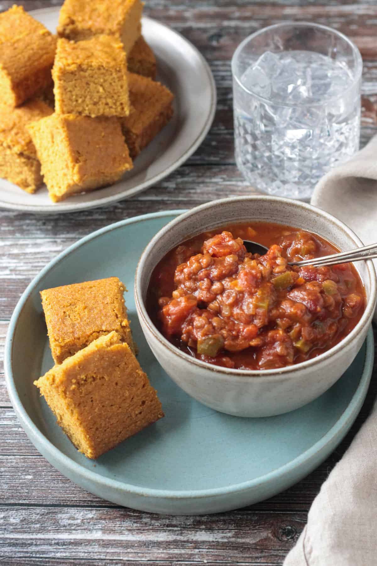 Two squares of cornbread on a plate next to a bowl of chili.