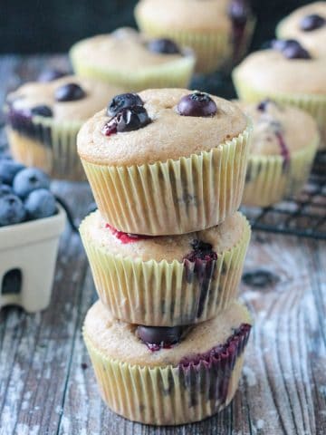 Stack of 3 vegan banana blueberry muffins in paper wrappers.