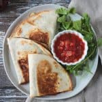 Overhead view of three halved vegan quesadillas next to a small bowl of salsa.