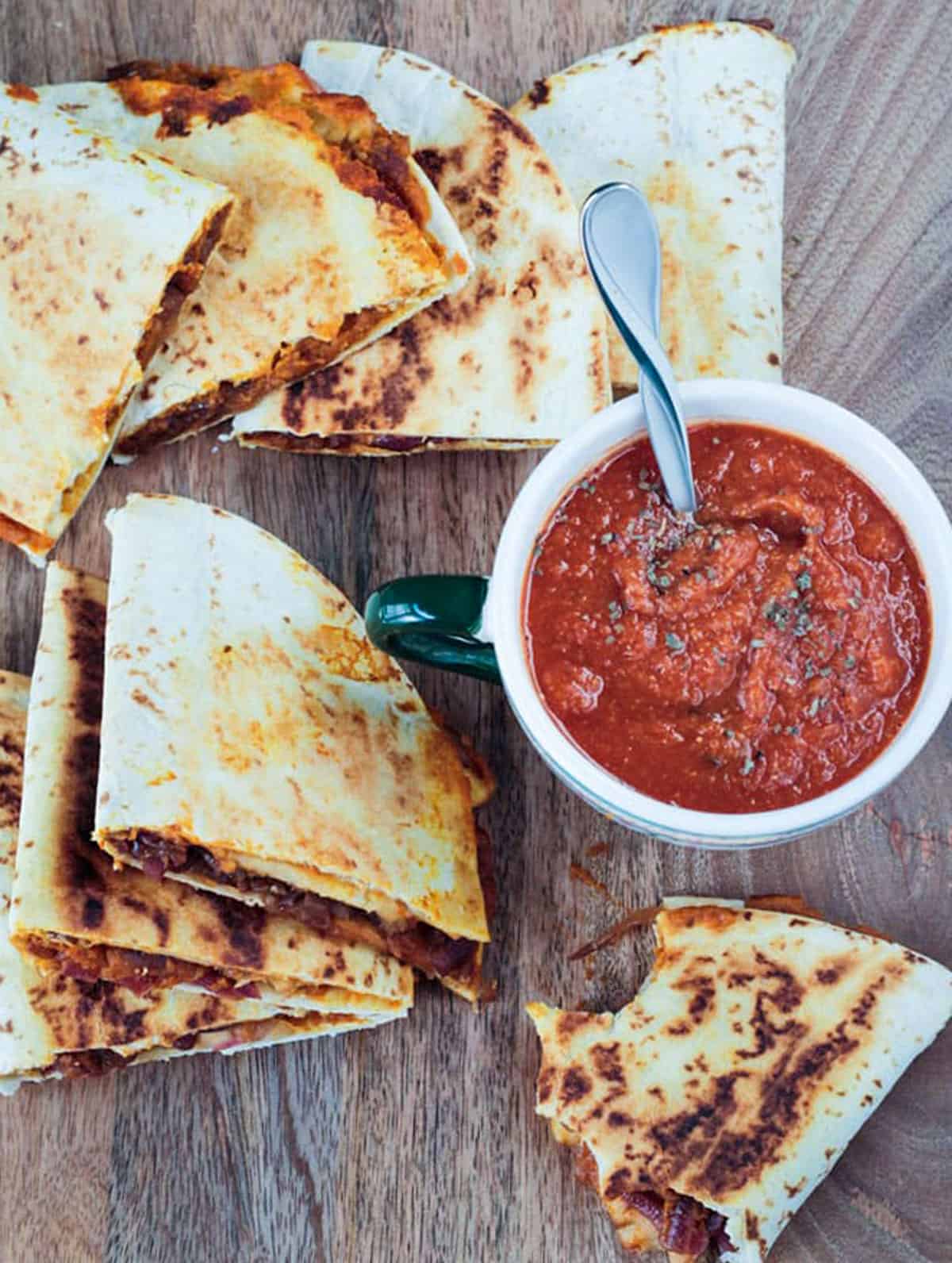 Several quesadilla halves surrounding a bowl of tomato soup.