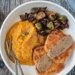 Two forks on a plate with butternut squash mash, brussels sprouts, vegan turkey cutlets, and gravy.