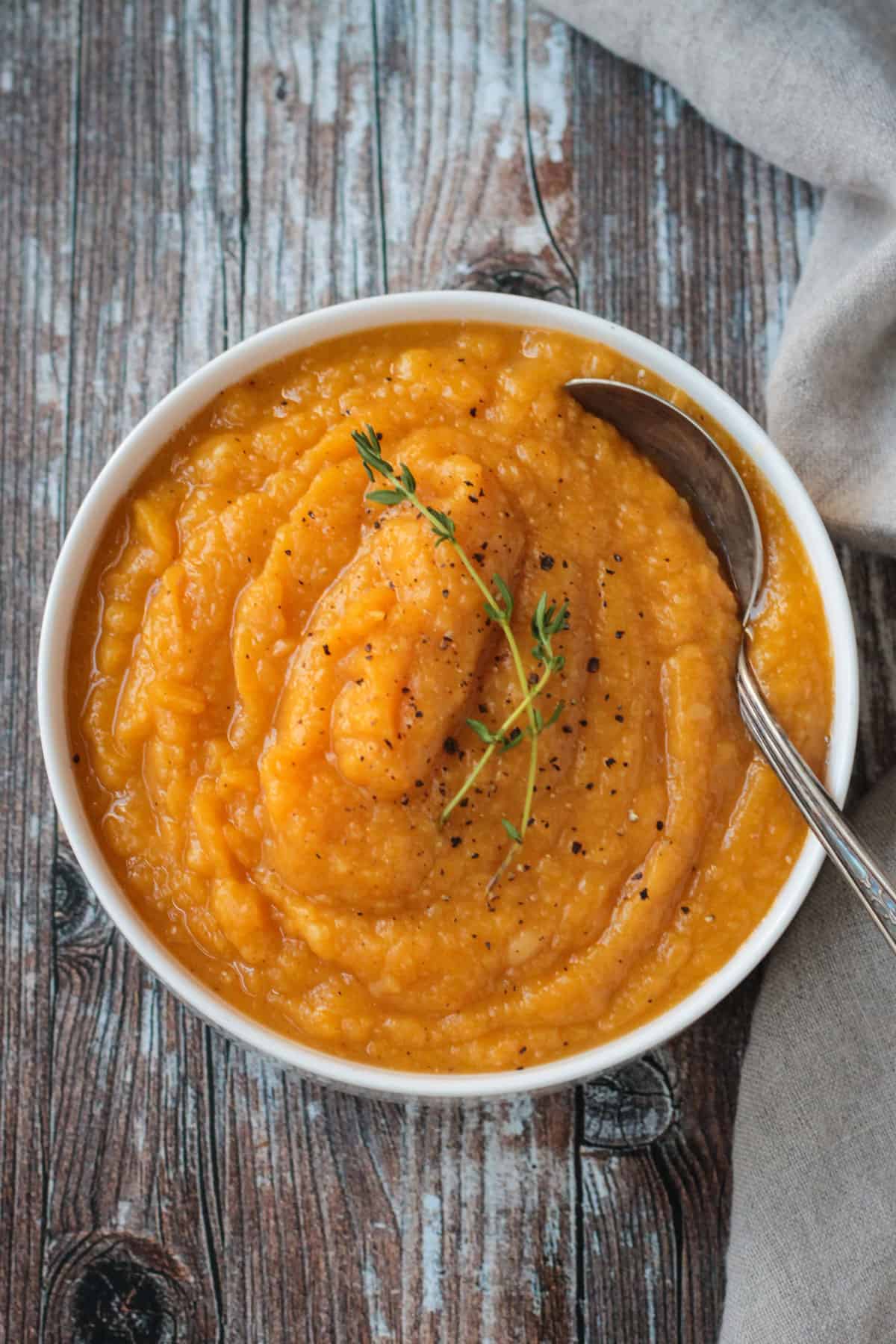 Overhead view of a bowl of butternut squash mash garnished with two sprigs of fresh thyme.