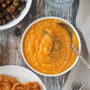 Bowl of mashed squash next to plates of other Thanksgiving foods.