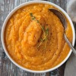 Overhead view of a bowl of butternut squash mash garnished with two sprigs of fresh thyme.