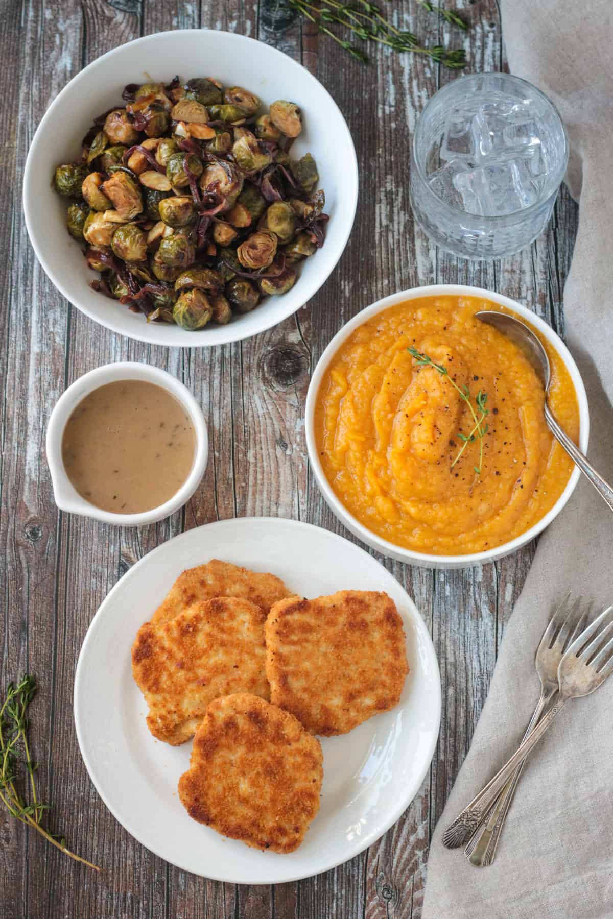 Brussels sprouts, butternut squash mash, vegan turkey cutlets, and gravy in individual bowls.